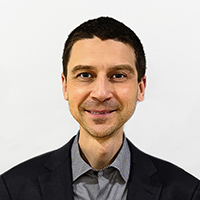 Headshot of Brian Corn wearing a gray polo shirt with a suitcoat and smiling